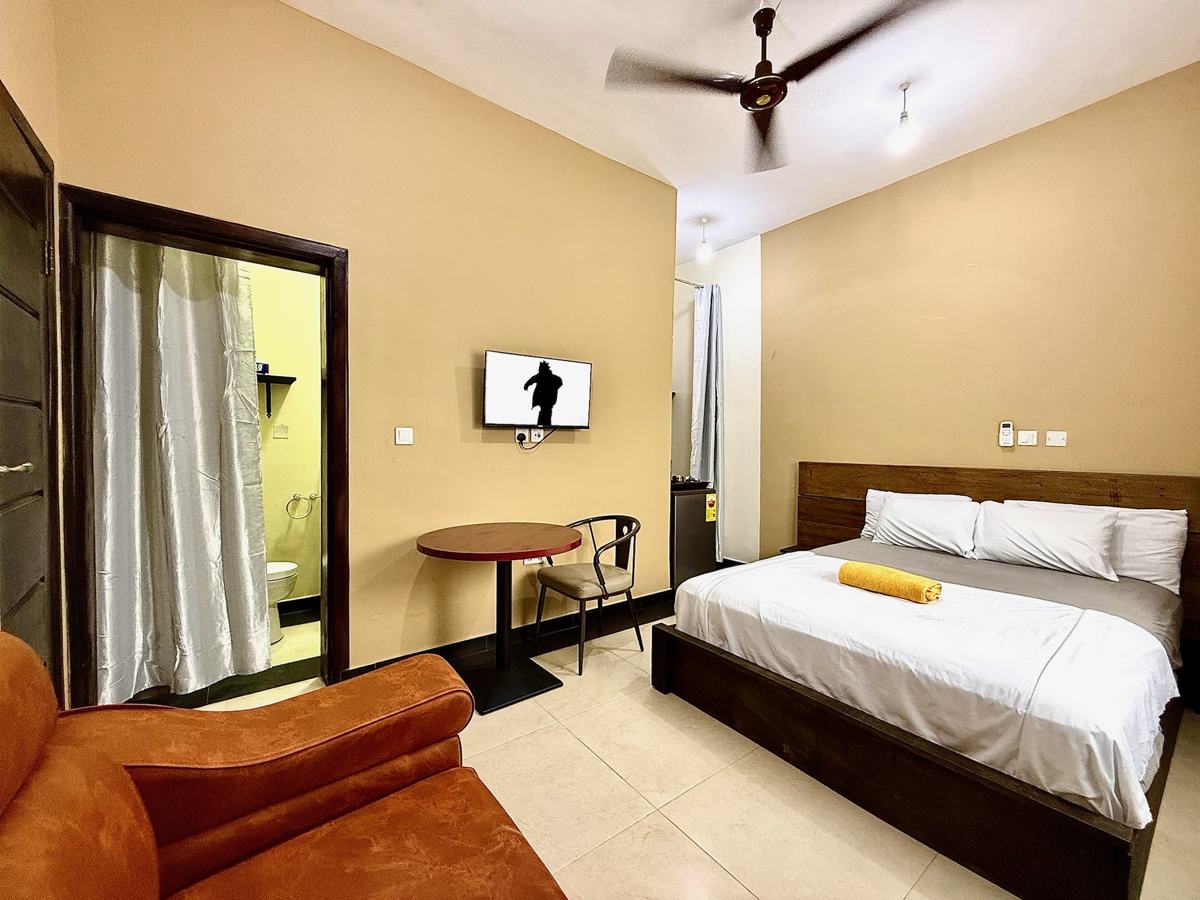 Queen studio suite with bed, orange sofa, table and TV